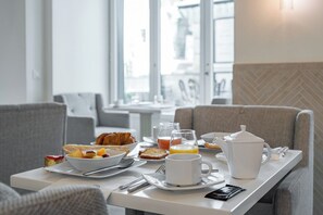 A breakfast setup with a bowl of fruit, croissant, coffee cup, and juice on a table. - Hotel Résidence Des Arts - Saint-Germain (Paris)