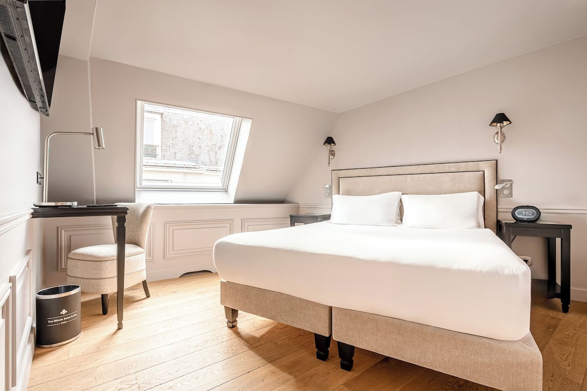 A bedroom with a large bed, a desk, a chair, a window, and a radiator.