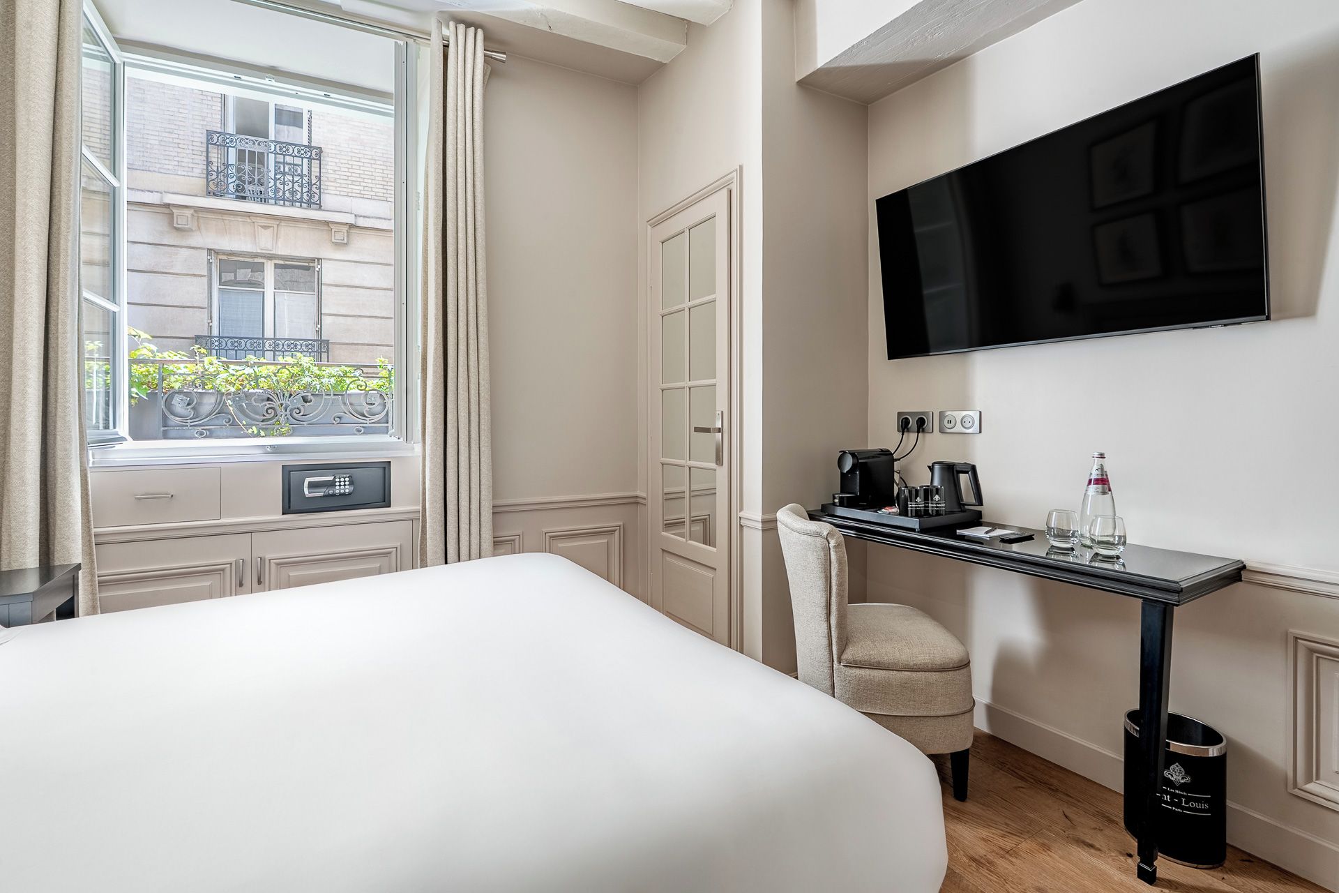 Una habitación de hotel con una cama, un escritorio con cafetera, televisión y ventana con vista a la calle.