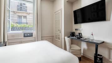 Una habitación de hotel con una cama, un escritorio con cafetera, televisión y ventana con vista a la calle.