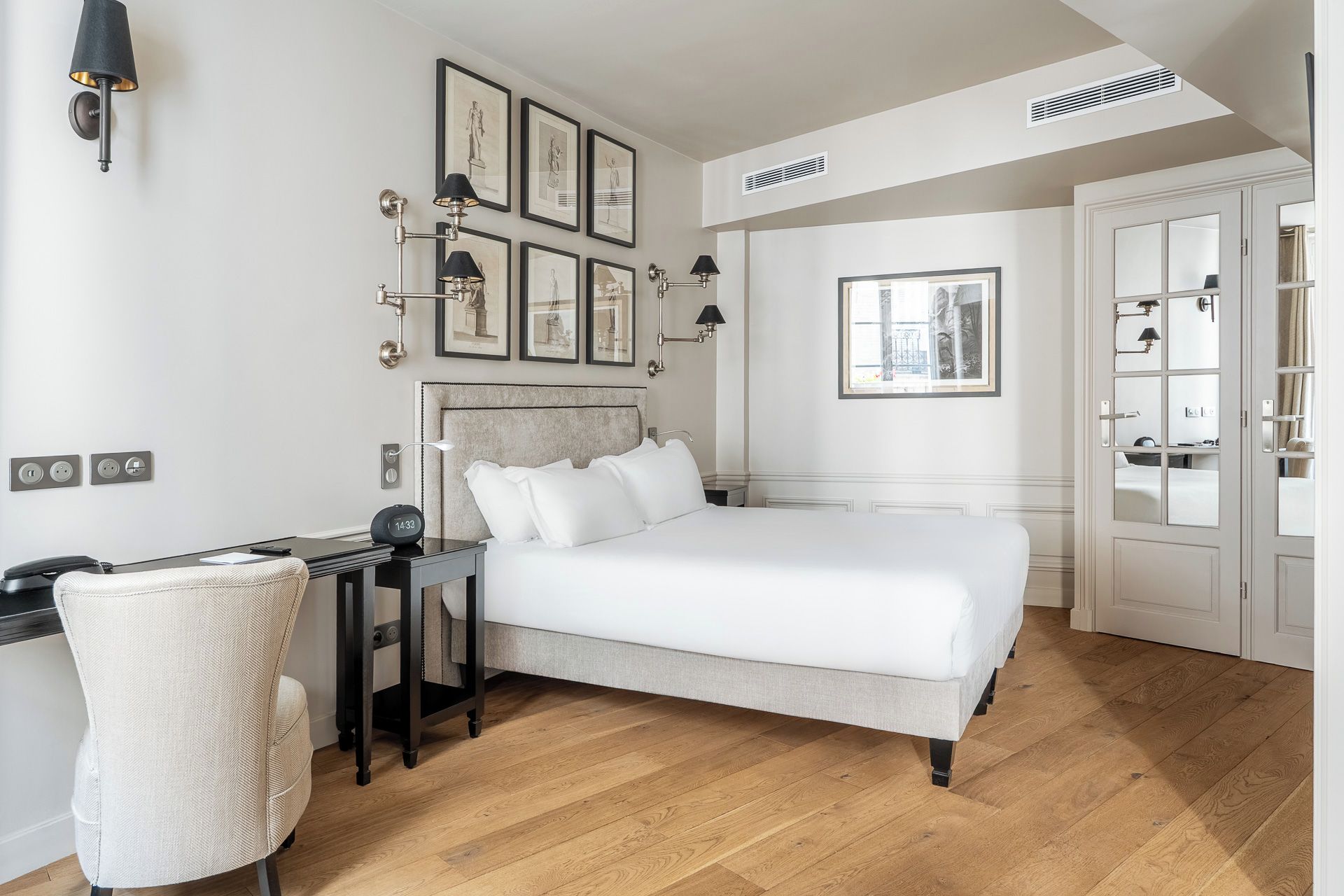 A hotel room with a bed, bedside table, lamp, chair, and wall-mounted artwork.