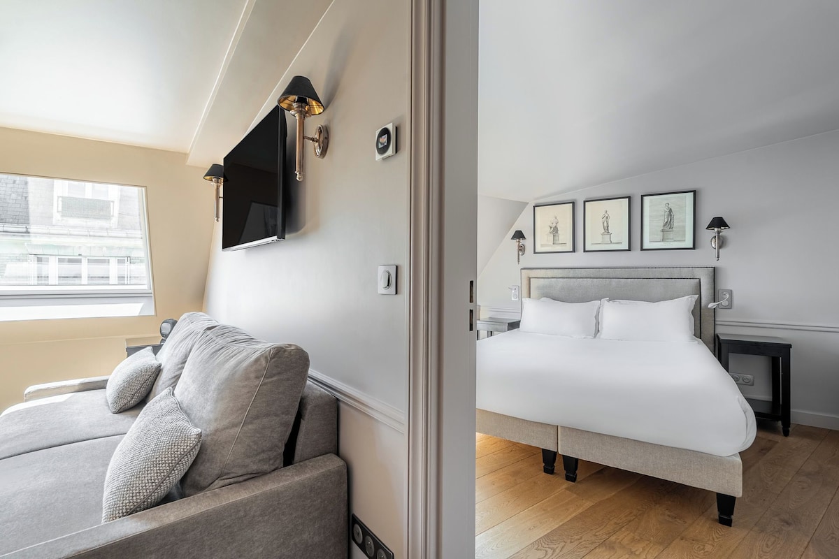 Habitación de hotel con cama, sofá, televisión y cuadros en la pared.