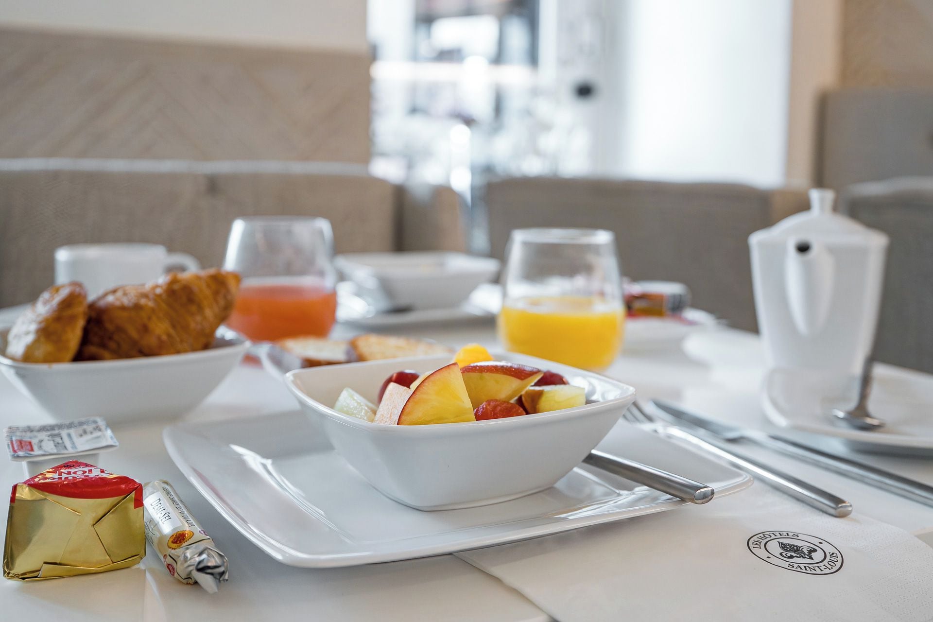 Desayuno con un bol de fruta, cruasanes y jugo en una bandeja.