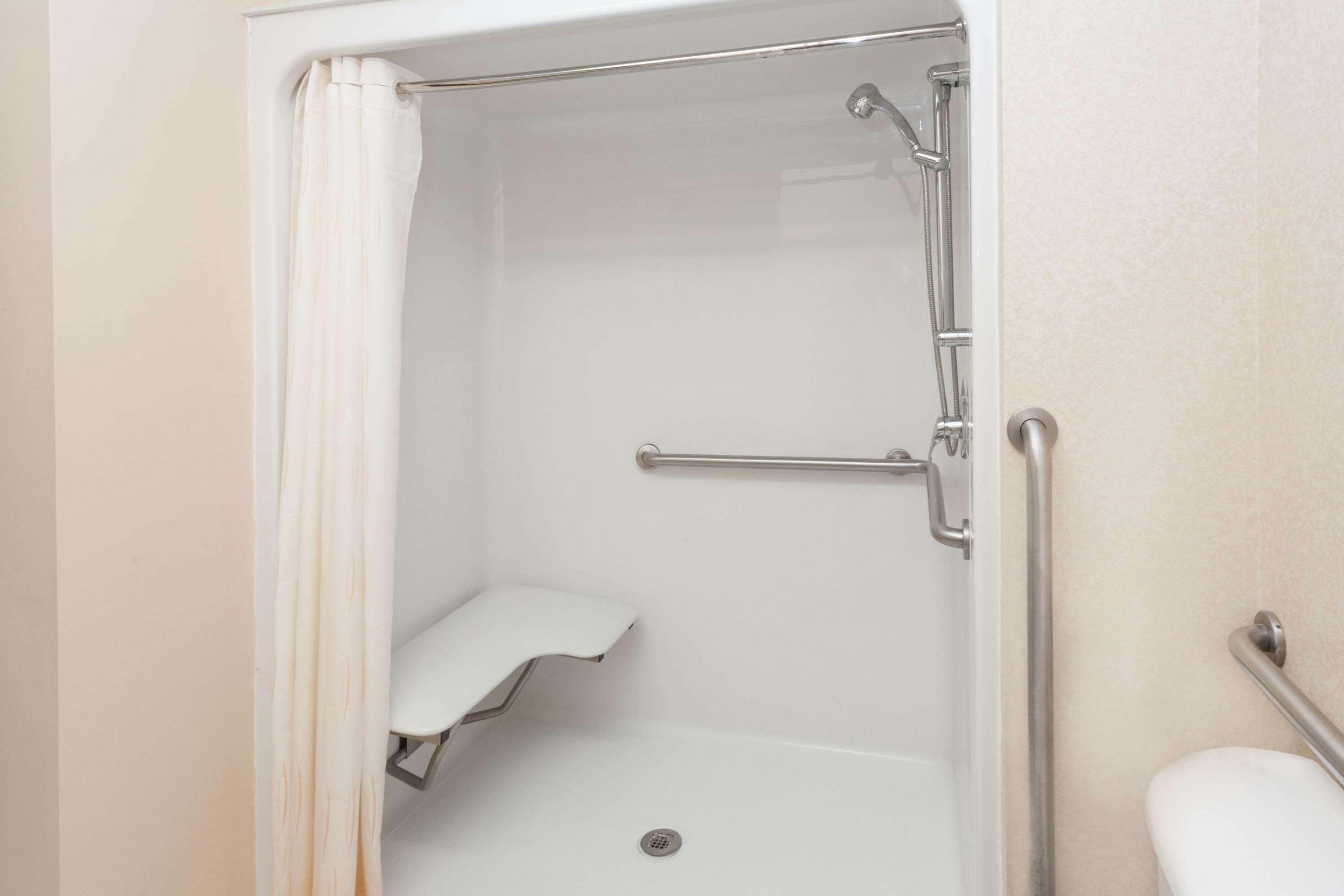 A walk-in shower with a white toilet, a grab bar, and a shower seat.