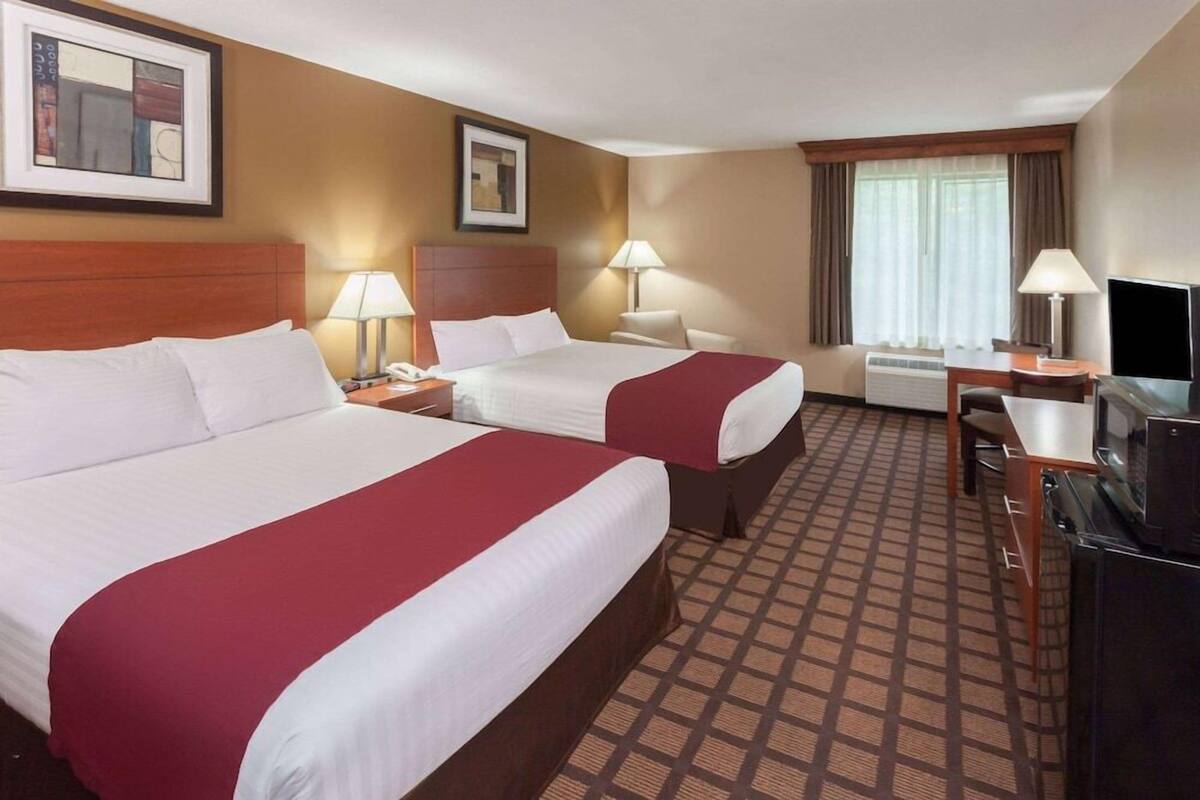 A hotel room with two beds, a desk, a TV, and a window with curtains.