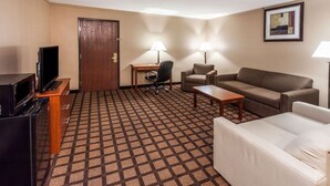 A hotel room with a sofa, a white armchair, a desk with a chair, a television, and a door. - Baymont by Wyndham New Buffalo (New Buffalo)