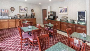 A hotel dining area with wooden cabinets, marble tables, and chairs. There are coffee machines and a refrigerator on the counter. - Baymont by Wyndham New Buffalo (New Buffalo)