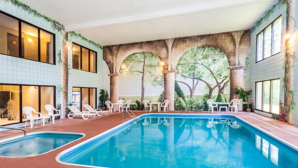 An indoor swimming pool with multiple lanes, surrounded by white lounge chairs and tables. - Baymont by Wyndham New Buffalo (New Buffalo)