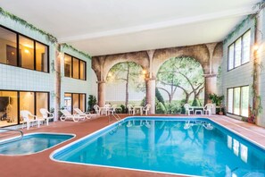 An indoor swimming pool with multiple lanes, surrounded by white lounge chairs and tables.