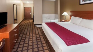 A hotel room with a large bed, a desk with a TV, a bathroom with a bathtub, and a patterned carpet. - Baymont by Wyndham New Buffalo (New Buffalo)