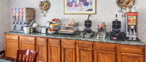 A breakfast bar with coffee machines, a fruit bowl, and a framed picture on the wall.