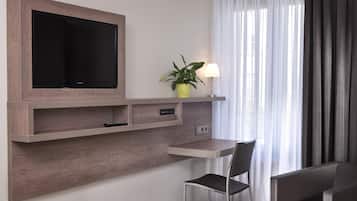 Une chambre moderne équipée d’un téléviseur fixé au mur, d’un bureau avec une chaise, d’une plante en pot et d’une lampe.