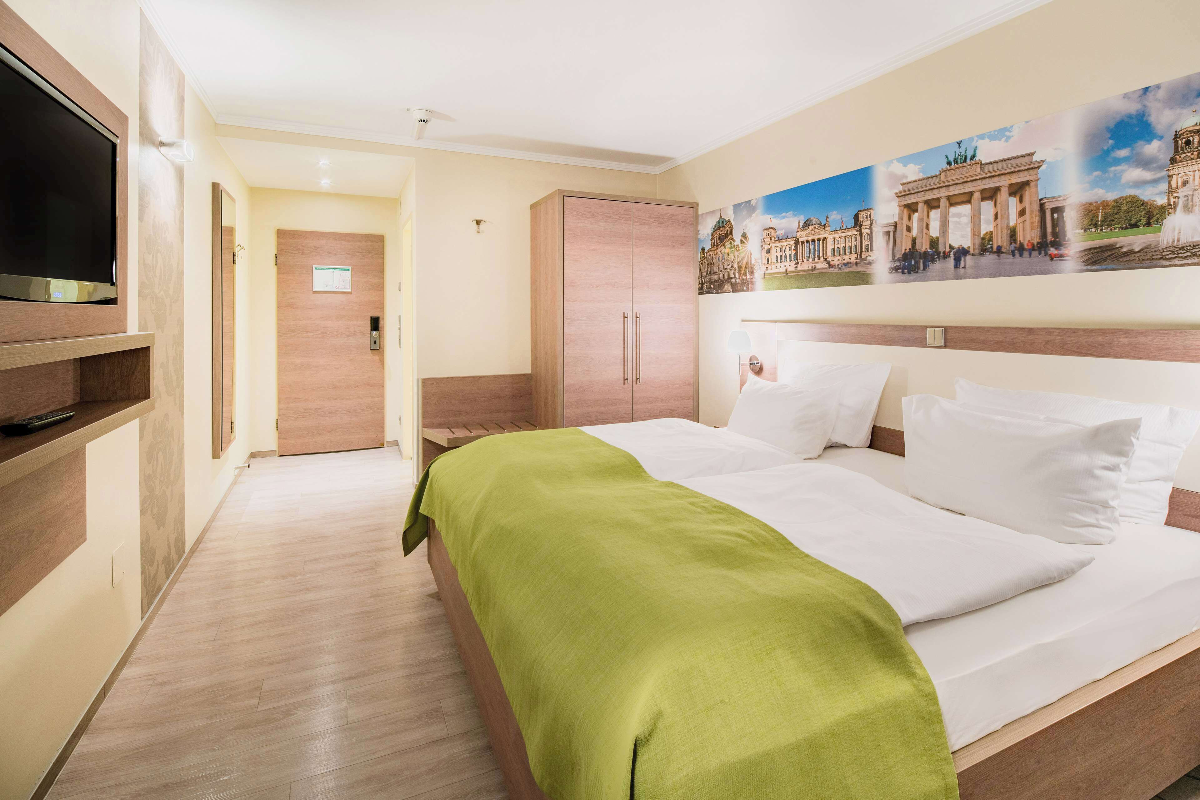 Ein Hotelzimmer mit Bett, Fernseher, Kleiderschrank und einem Gemälde eines historischen Gebäudes.