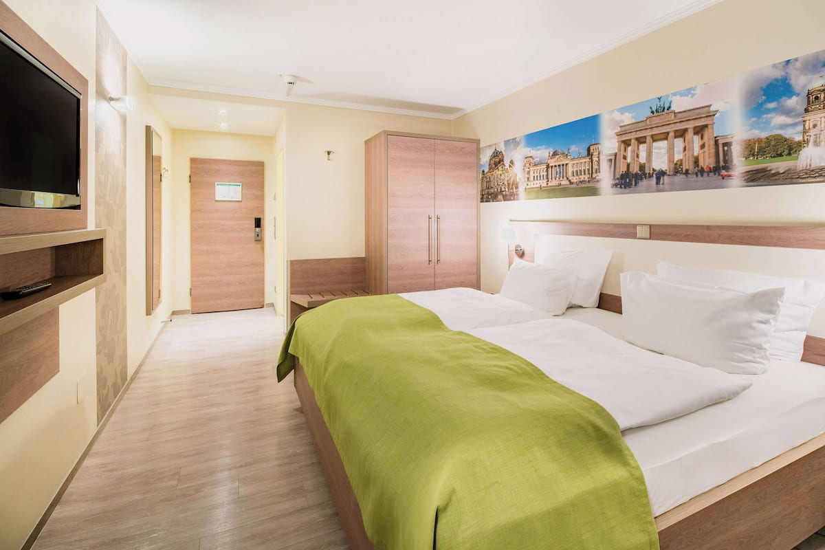 Ein Hotelzimmer mit Bett, Fernseher, Kleiderschrank und einem Gemälde eines historischen Gebäudes.