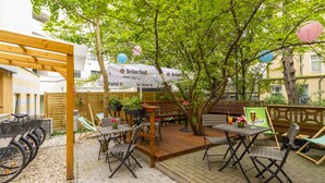 Een terras met tafels en stoelen, omringd door bomen en overdekt door een luifel.