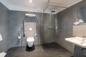 Une salle de bain moderne avec une douche à parois de verre, des toilettes blanches et un lavabo surmonté d’un miroir.
