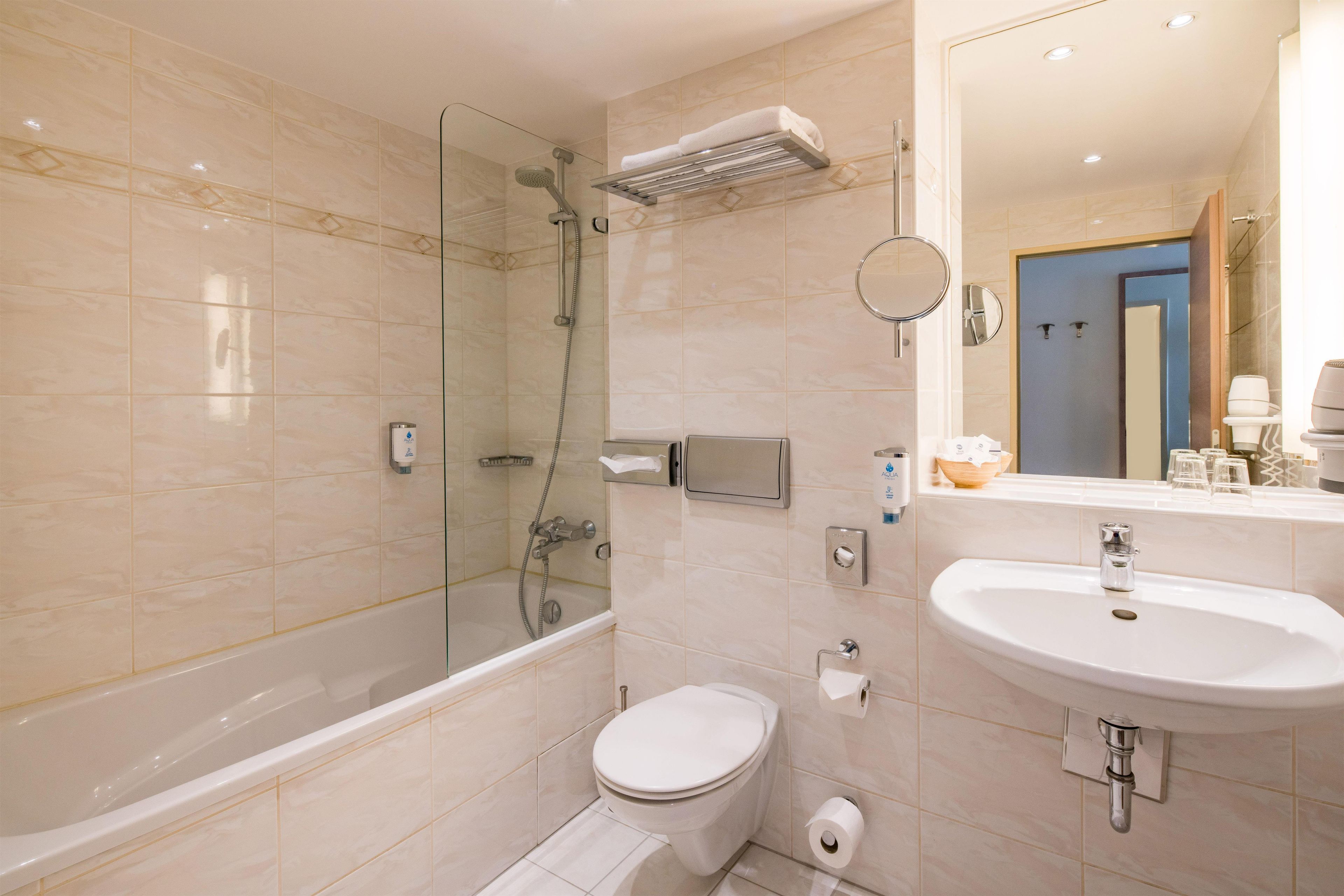Un baño moderno con ducha envuelta en vidrio, inodoro blanco y lavamanos con espejo.