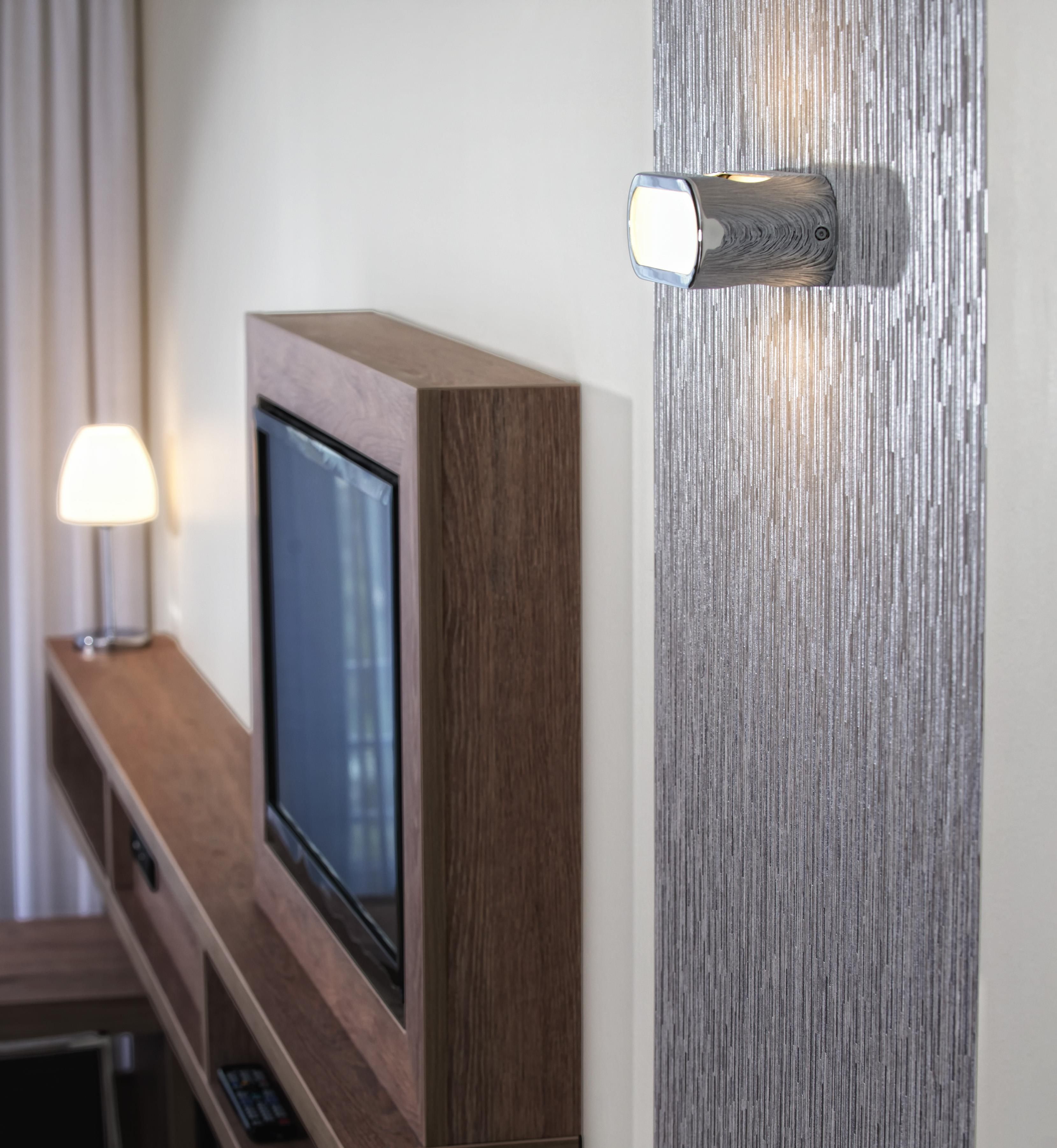Un televisor sobre un soporte de madera, una lámpara de pared y una lámpara en una mesa.
