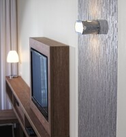 Un televisor sobre un soporte de madera, una lámpara de pared y una lámpara en una mesa.