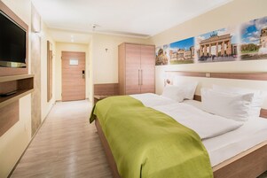 A hotel room with a bed, a television, a wardrobe, and a painting on the wall.