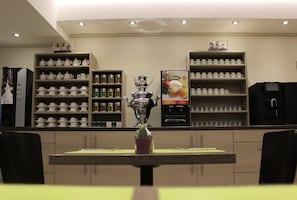 Een restaurant met een toonbank, planken met theepotten en kopjes, en een menukaartstandaard.