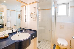Un baño moderno con ducha envuelta en vidrio, un lavamanos blanco con encimera azul y un inodoro.