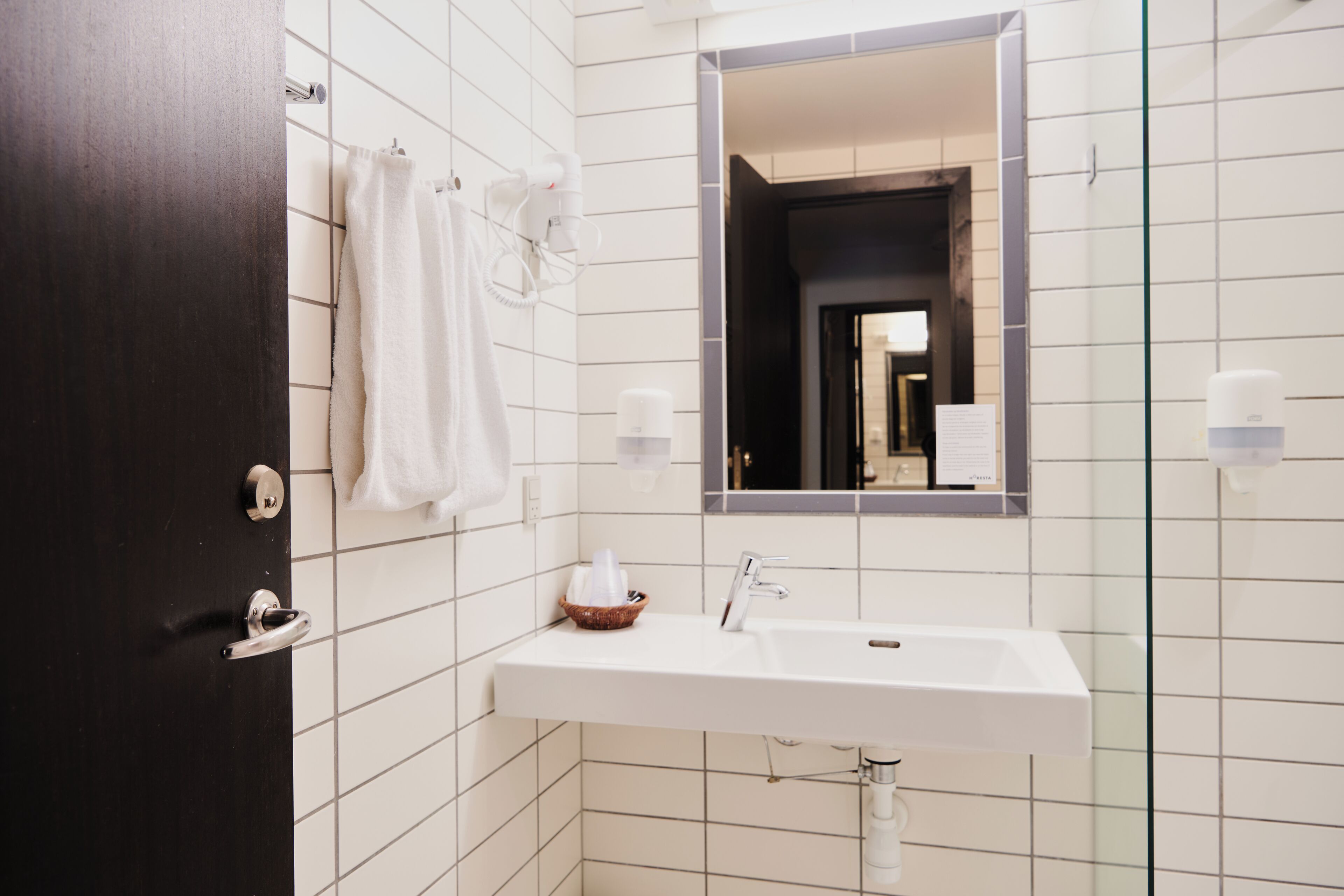 A bathroom with a white sink, a mirror, a towel rack, and a dark door.