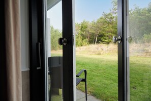 A view through a glass door leading to an outdoor area with a grassy lawn and trees.