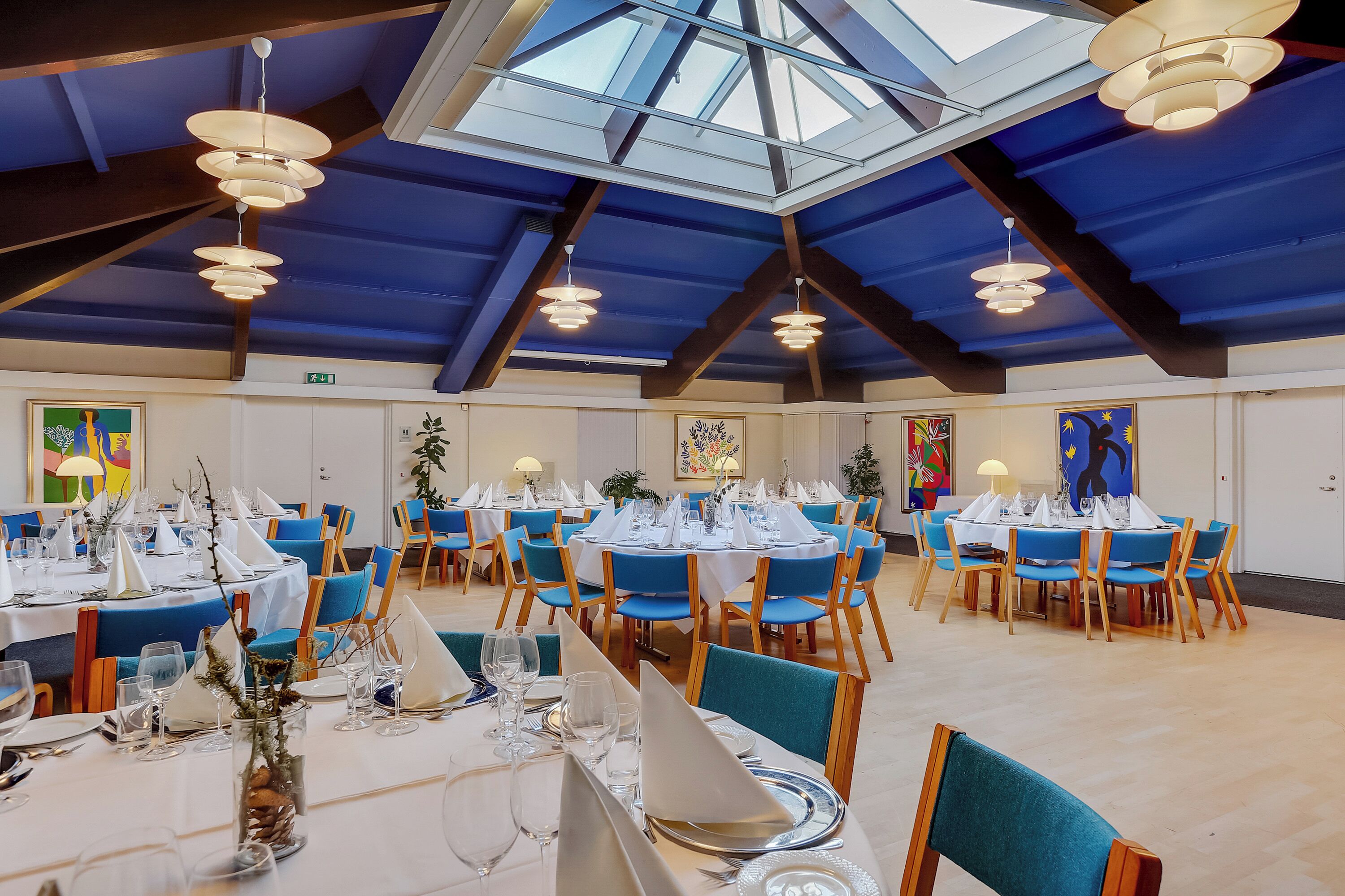 A spacious dining area with round tables set for multiple guests, featuring blue chairs and white tablecloths.