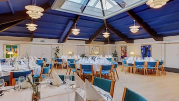 Un vaste espace dédié à la salle à manger, avec des tables rondes disposées pour accueillir plusieurs convives, agrémenté de chaises bleues et de nappes blanches.