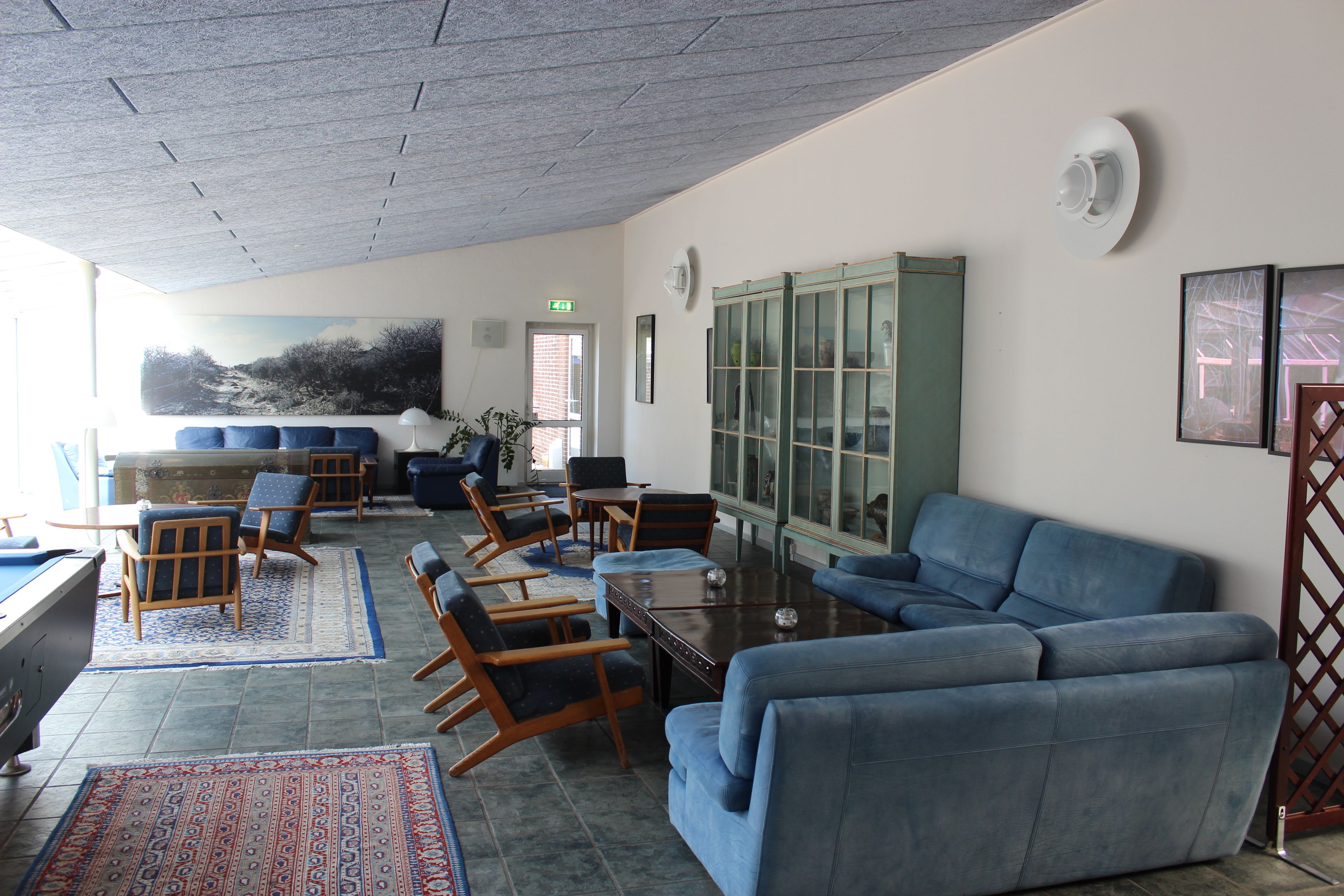 A spacious lobby with a blue sofa, wooden chairs, a coffee table, and a large cabinet with glass doors.