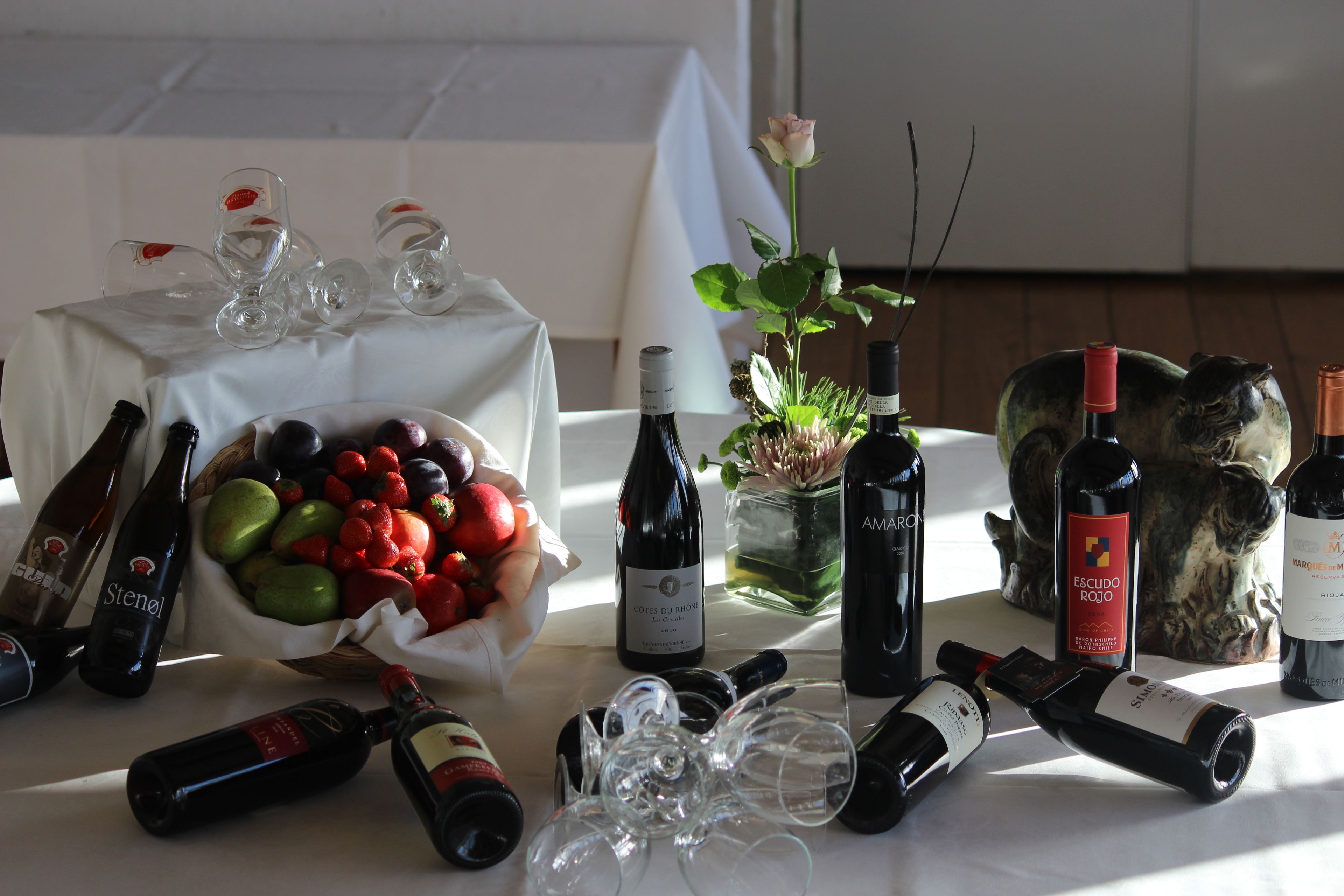 A table with wine bottles, glasses, and a bowl of fruit.