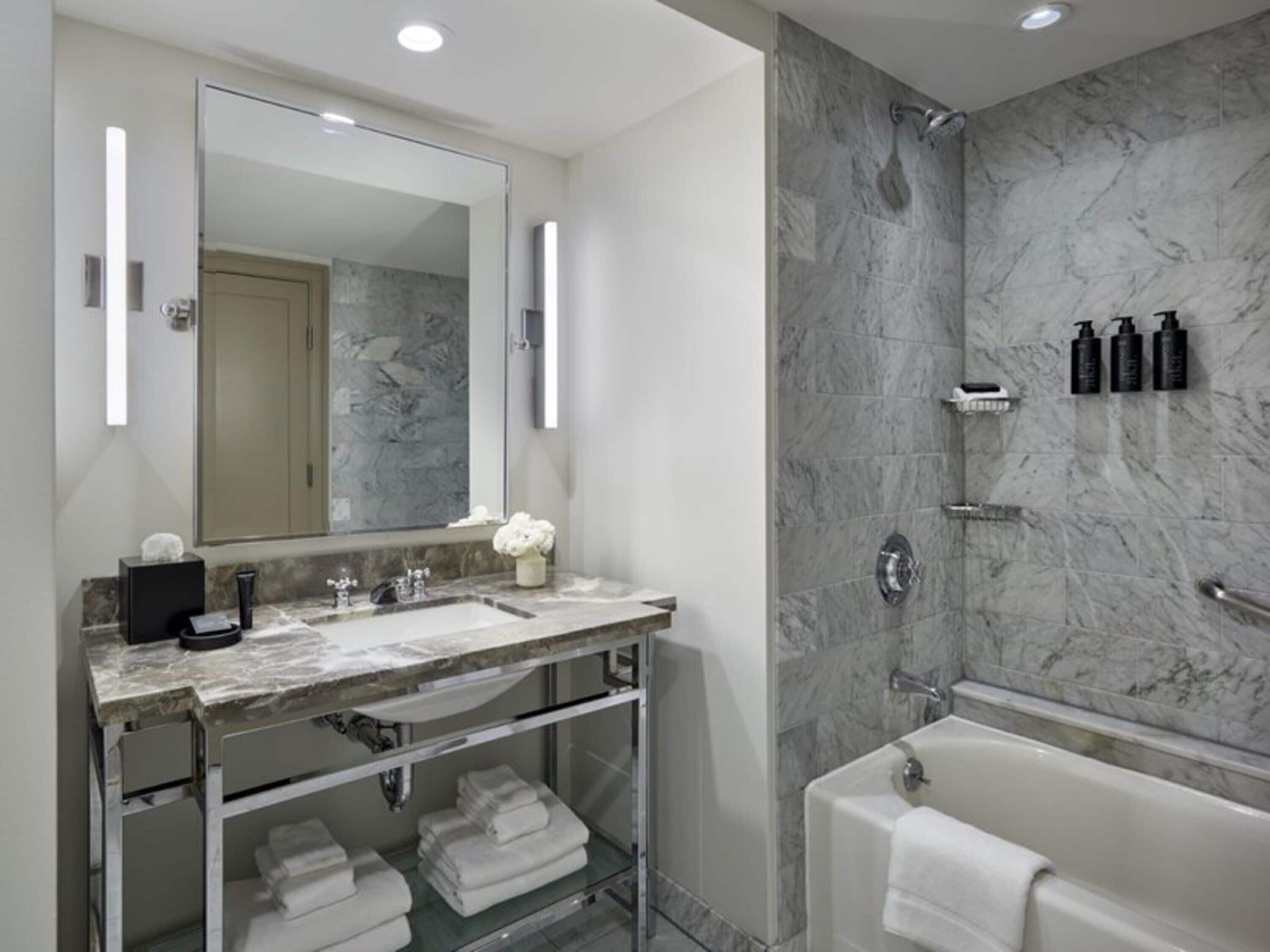 A modern bathroom with a marble sink, a large mirror, a glass shower enclosure, and a bathtub.