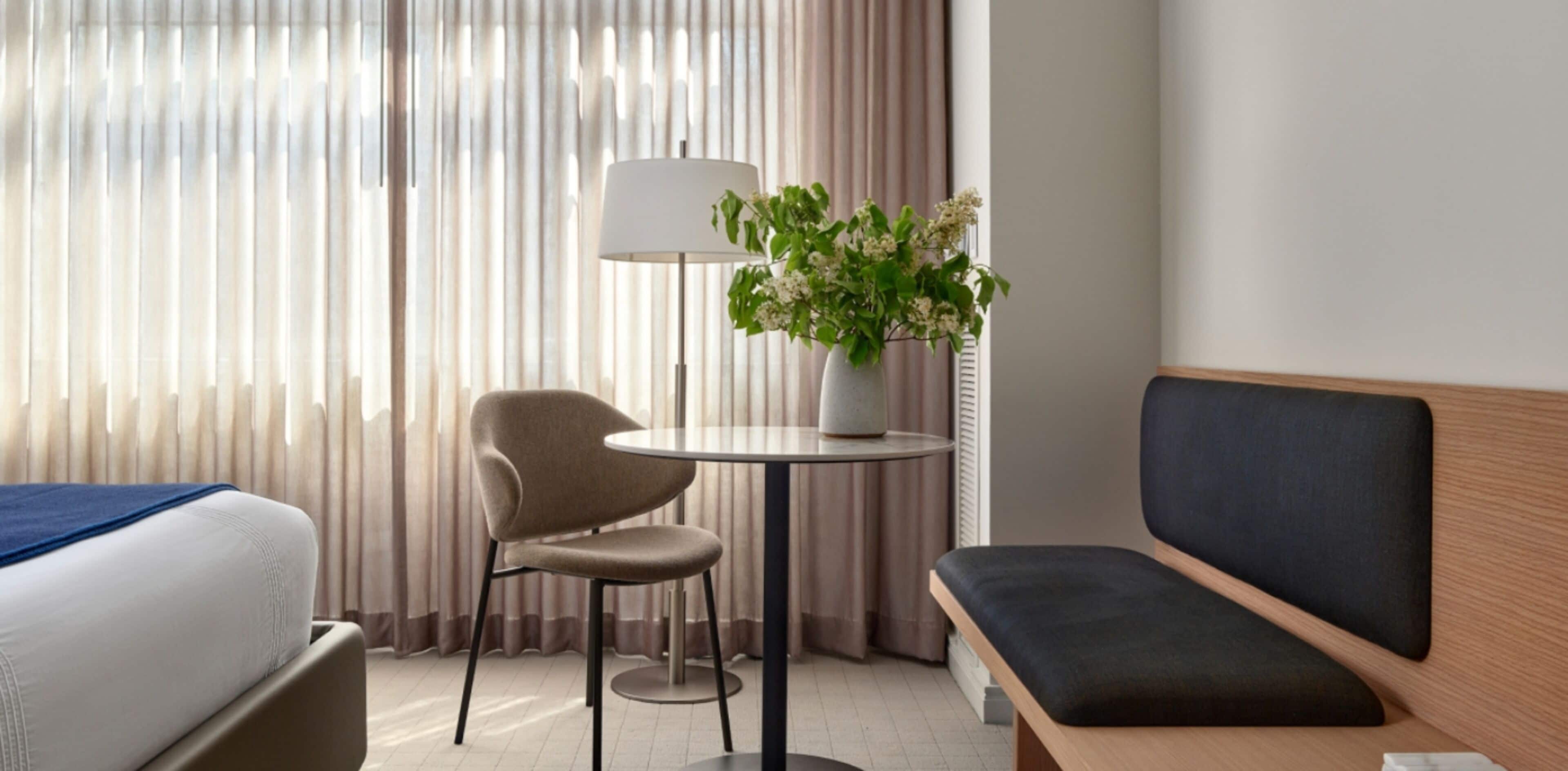Een hotelkamer met een bed, een stoel, een kleine tafel met een lamp en een bloemenvaas, en een bank.