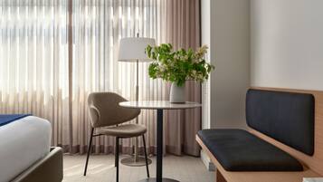 Een hotelkamer met een bed, een stoel, een kleine tafel met een lamp en een bloemenvaas, en een bank.