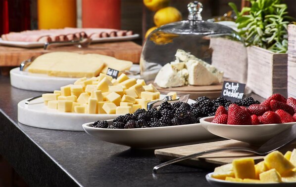 A buffet with various cheeses, blackberries, strawberries, and a glass container of blue cheese.
