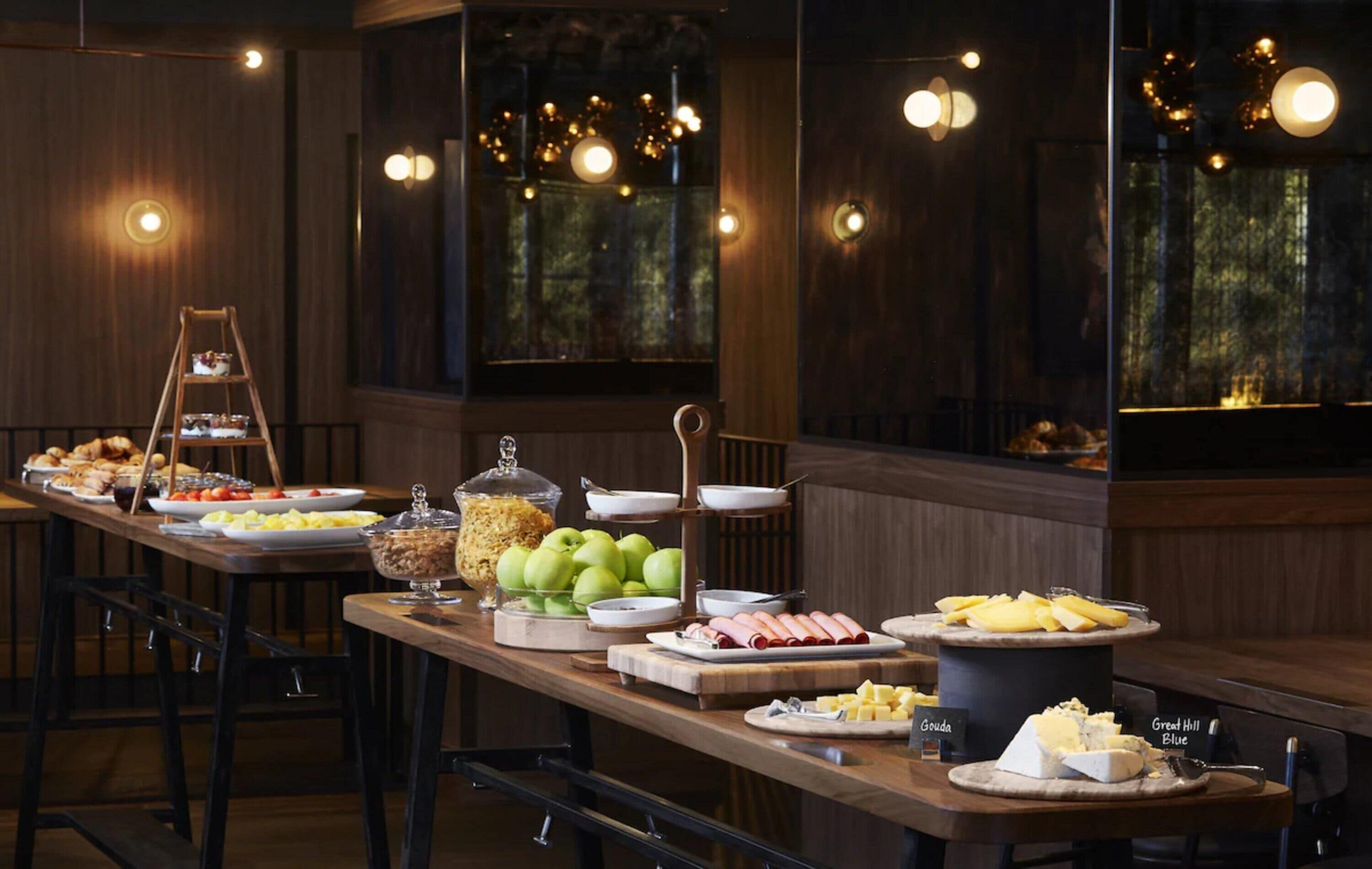 A buffet with various food items, a ladder, and a view of the outdoors through large windows.