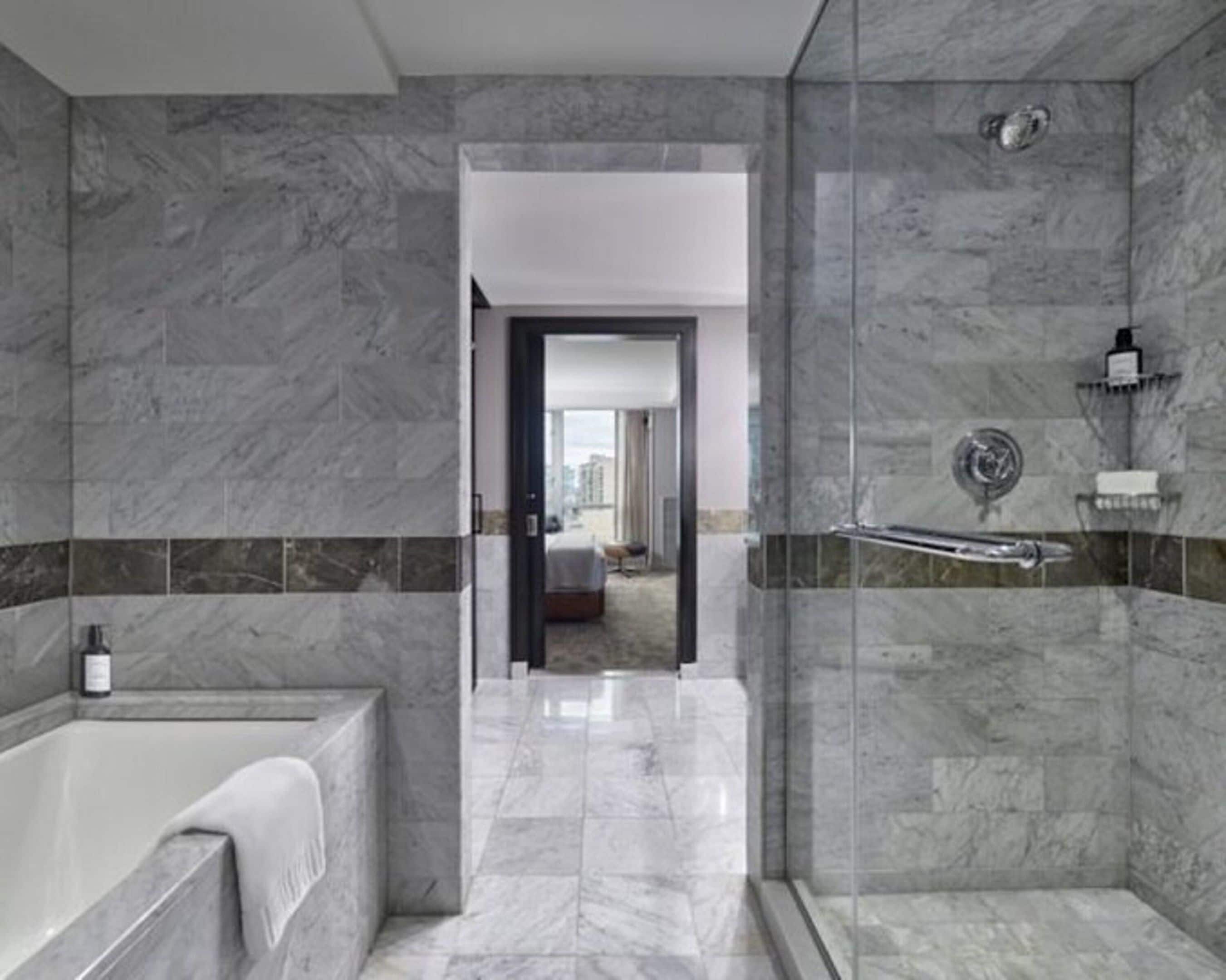 A modern bathroom with a bathtub, a shower with a glass door, and a view of a bedroom through an open door.