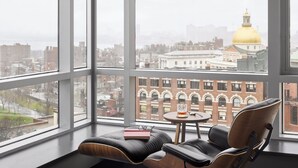 Une chambre moderne dotée de grandes fenêtres, d’un canapé en cuir, d’une petite table et offrant une vue sur le paysage urbain, notamment un bâtiment imposant surmonté d’un dôme doré.