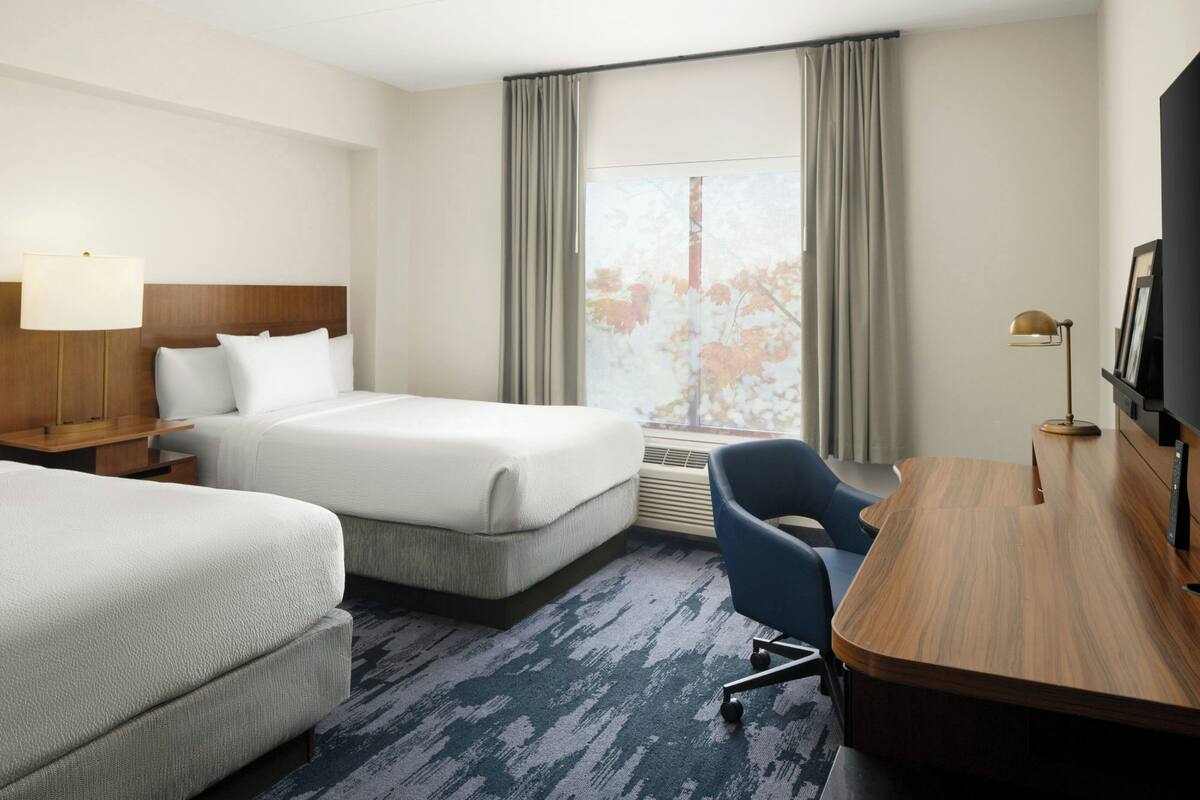 Une chambre d’hôtel avec deux lits, un bureau, une chaise, une télévision et une fenêtre avec des rideaux.