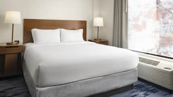 A hotel room with a large bed, two bedside tables with lamps, a window with a view of trees, and a wall-mounted air conditioner.