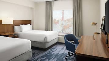 A hotel room with two beds, a desk, a chair, a TV, and a window with curtains.