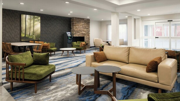 A modern hotel lobby with a large dining table, comfortable seating, a fireplace, and large windows.