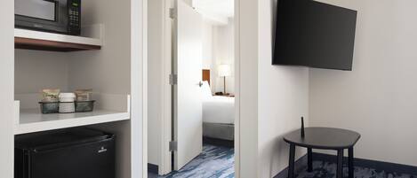A hotel room with a microwave, refrigerator, and a flat-screen TV mounted on the wall.