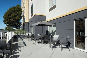 An outdoor patio with modern chairs and tables, a large umbrella, and a building with a glass door.