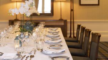 A dining table set with multiple plates, cutlery, and glasses, flanked by chairs and lamps.
