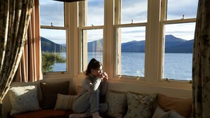 A person sitting on a bench by a window overlooking a body of water and mountains. - Loch Fyne Hotel And Spa (Inveraray)