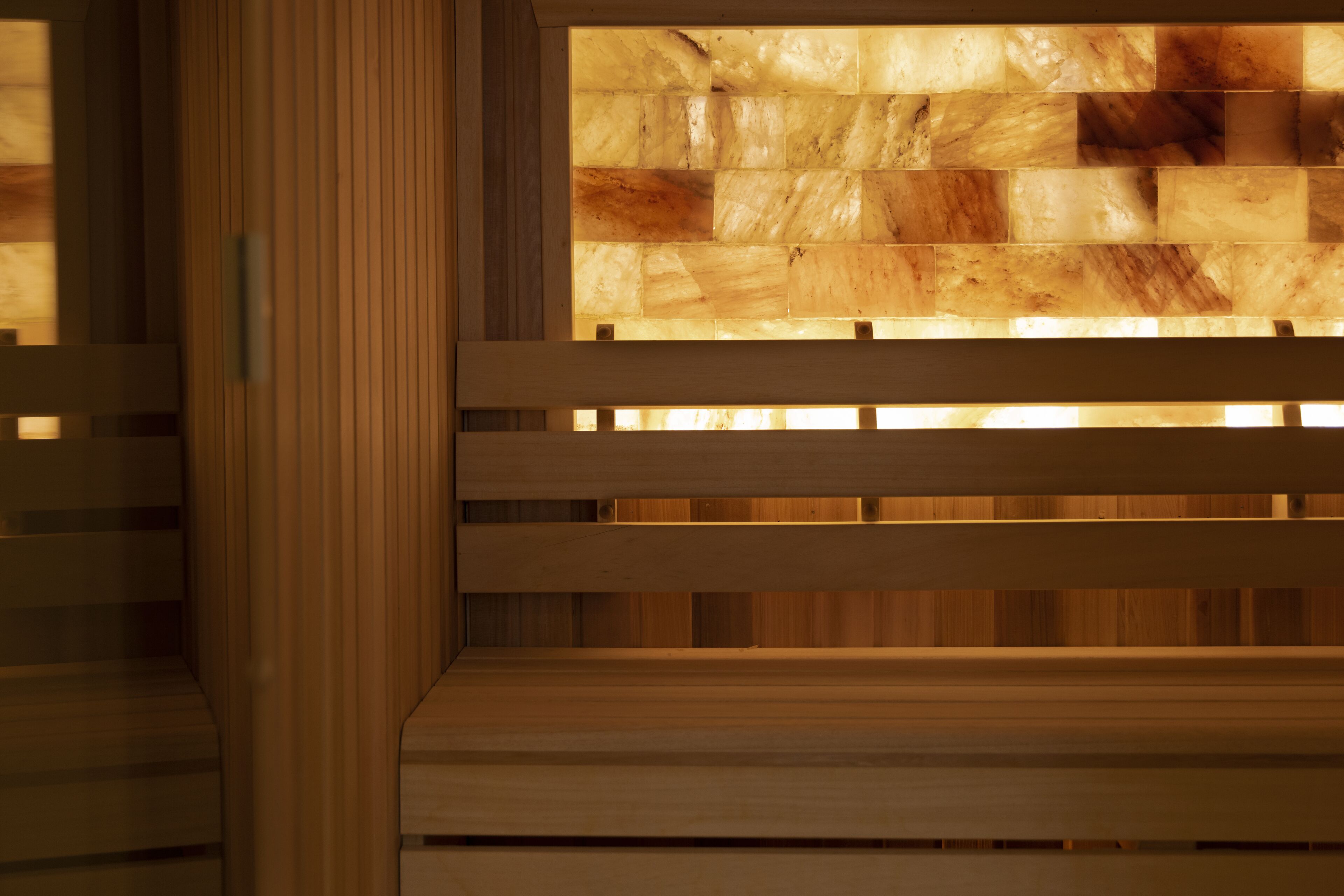 A wooden bench with a backrest and a wall with a patterned design.