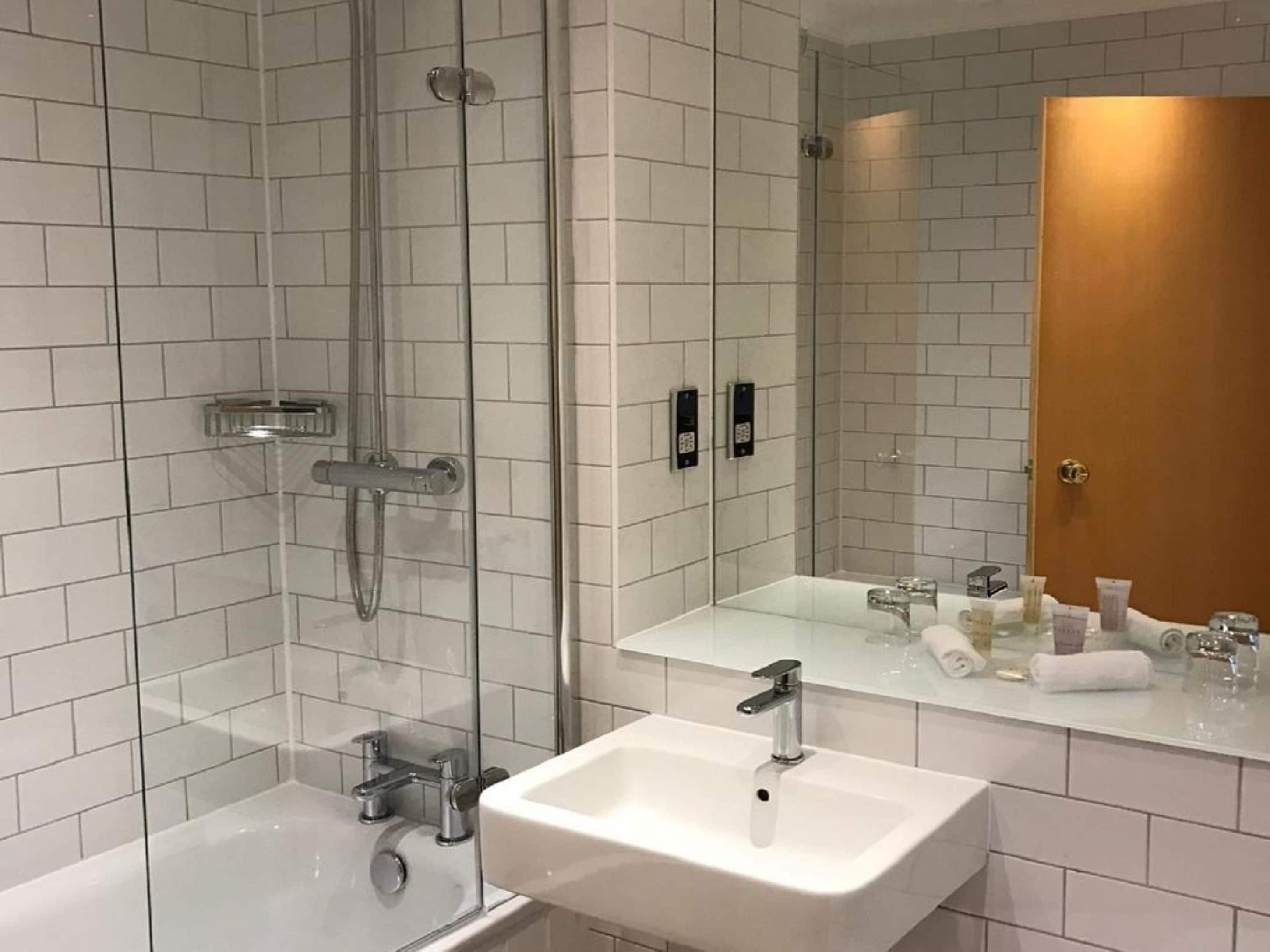 A modern bathroom with a glass shower enclosure, a white sink, and a large mirror reflecting the room.