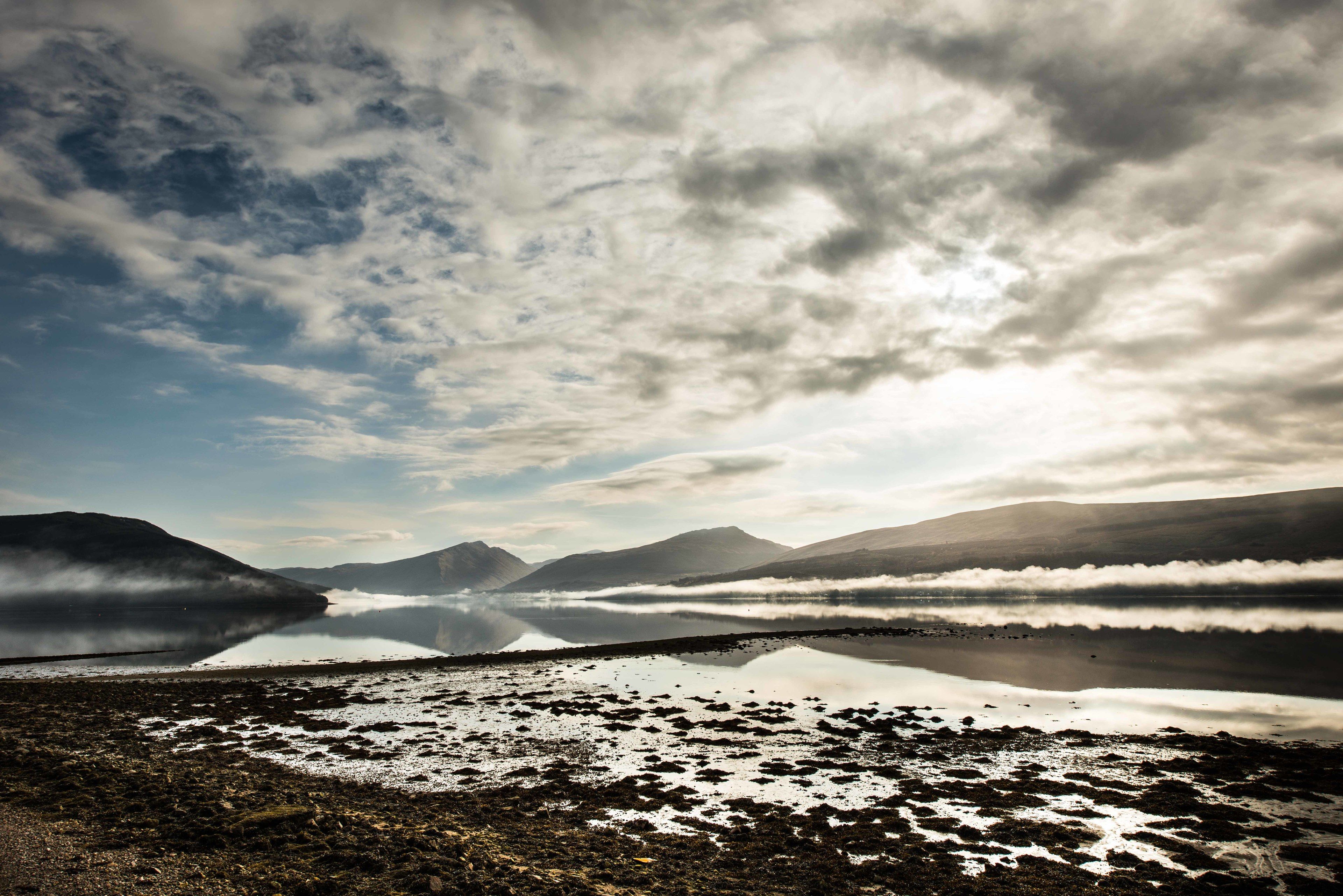 A lake with mountains in the background and a cloudy sky.